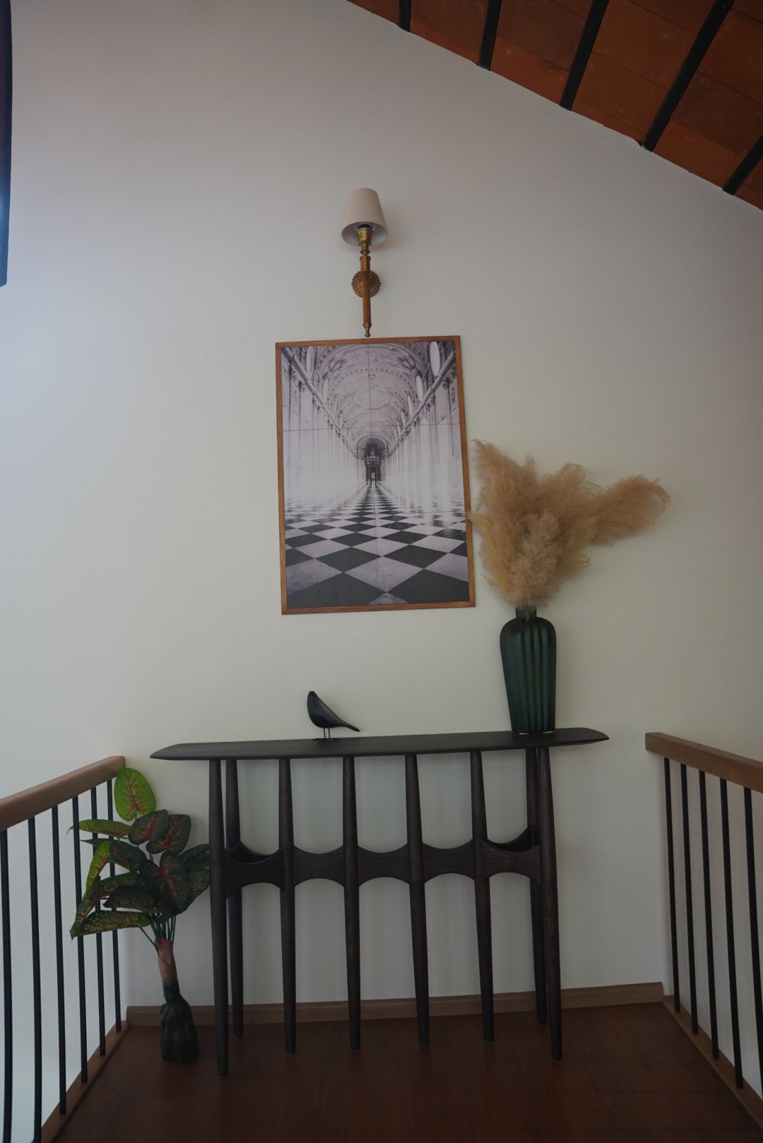 Sculpted dark timber console under a brass wall sconce on a stair landing